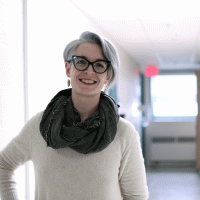 person with short hair and glasses smiling in a hospital hallway